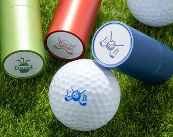 Könnte beinhalten: Golfbälle und zylindrische Behälter auf grünem Gras. Die Golfbälle haben blaue Logos mit den Buchstaben "E" und "B". Die Behälter sind grün, rot und blau, jeder mit einem anderen Namen oder Logo.