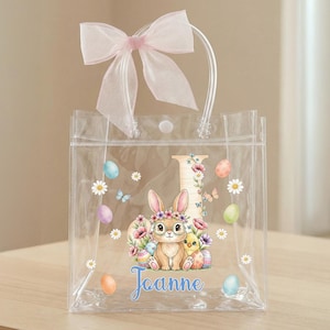 May include: Clear Easter-themed tote bag with a pink bow and clear handles. The bag features a bunny, chick, and Easter eggs design with the name "Joanne" in blue script. Decorative flowers and butterflies are also present.