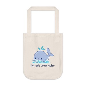 May include: Cream-coloured tote bag with a cartoon whale illustration in light blue, with water splashes. The text "hot girls drink water" is below the whale. The bag has two handles and is made of a canvas-like material.