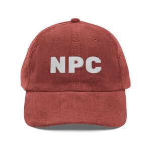May include: A red-brown corduroy baseball cap with the white letters "NPC" embroidered on the front. The cap has a curved brim and a button on top.