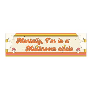 Könnte beinhalten: Rechteckiges Schild mit cremefarbenem Hintergrund und Retro-Design. Das Schild zeigt den Text "Mentally, I'm in a Mushroom circle" in orangefarbener Schrift. Das Design umfasst orange, gelbe und rosa Streifen sowie Pilz- und Sternillustrationen.