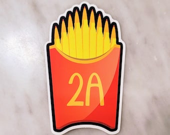 Könnte beinhalten: Ein gestanzter Aufkleber mit einem roten Karton, der mit gelben, patronenförmigen Objekten gefüllt ist, die wie Pommes frites angeordnet sind. Auf dem roten Karton ist vorne der Text 2A in Gelb aufgedruckt. Das Design hat einen dicken weißen Rand.