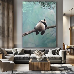 May include: A black and white panda bear sitting on a branch with a blurred green and blue background.