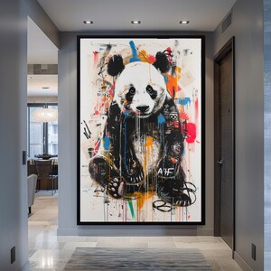 May include: A colourful abstract painting of a panda bear with black and white fur. The panda is wearing a blue and black jacket with graffiti-style text and symbols. The background is a white canvas with splashes of colour, including red, orange, yellow, green, and blue.