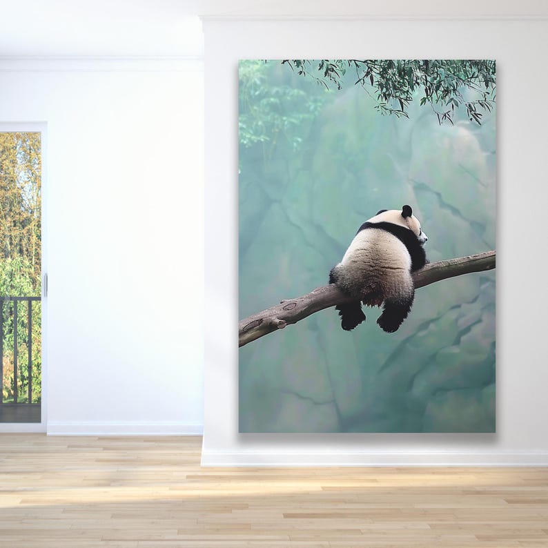 May include: A black and white panda bear sits on a branch with its back to the camera. The panda is looking to the right and has its head resting on the branch. The background is a blurry green and blue.