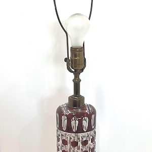 Puede incluir: Lámpara de mesa vintage con cuerpo de cristal tallado rojo rubí y detalles en latón. La lámpara presenta una base decorativa y un soporte de pantalla metálico. La lámpara está rematada con una bombilla esmerilada y una pieza decorativa.