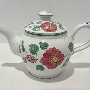 May include: White ceramic teapot with a lid, decorated with red, purple, and yellow floral patterns and green leaves. The teapot has a curved spout and handle, and a matching floral design on the lid.