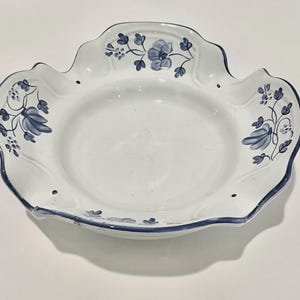 May include: White ceramic serving dish with a scalloped edge and blue floral design. The rim is outlined in blue, and the dish features hand-painted blue flowers and leaves. A decorative piece for serving.