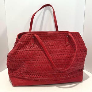 May include: A red tote bag with a woven design. The bag has two handles and a shoulder strap. The bag is made of a textured material and has a rectangular shape. The bag is approximately 14 inches wide and 10 inches tall.