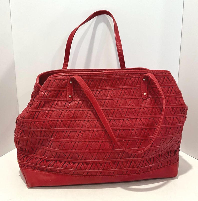 May include: A red tote bag with a woven design. The bag has two handles and a shoulder strap. The bag is made of a textured material and has a rectangular shape. The bag is approximately 14 inches wide and 10 inches tall.