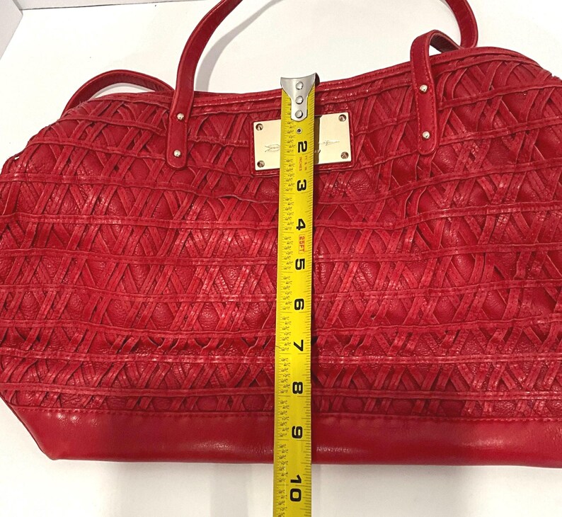 May include: Red handbag with woven texture and dual handles. The bag has a rectangular shape and measures approximately 10 inches in height. Gold-toned metal accents and a rectangular nameplate are visible on the front.