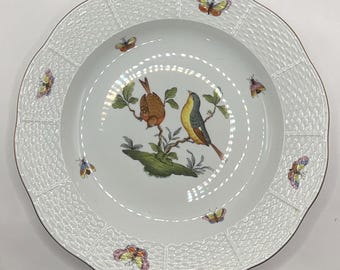 May include: White ceramic plate with a textured rim and a decorative bird and butterfly design. The plate features a central illustration of two birds perched on a branch, surrounded by colorful butterflies. The rim has a woven pattern.