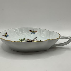 May include: A white porcelain dish with a gold rim and a butterfly design. The dish has a handle and is shaped like a leaf.