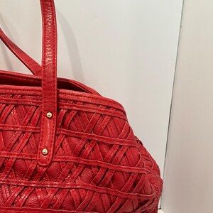 May include: Red leather tote bag with a woven design. The bag features two top handles and gold-colored rivets. The bag's body has a textured, crisscross pattern.