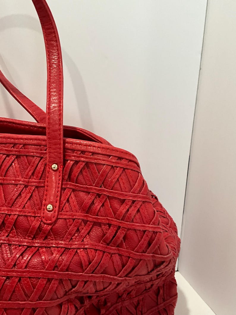 May include: Red leather tote bag with a woven design. The bag features two top handles and gold-colored rivets. The bag's body has a textured, crisscross pattern.