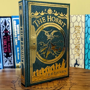 May include: A white ceramic mug with a black handle and the text "But First, Coffee" in a black, handwritten-style font. The mug is on a white surface.