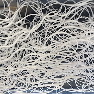 May include: A close-up of a white, tangled mass of string or yarn. The string is in a clear container, and the background is a dark gray.