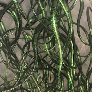 May include: A close-up of a bundle of green glitter wire. The wire is twisted and tangled, creating a textured and sparkly effect.
