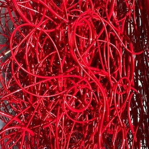 May include: A close-up view of a dense network of glossy, bright red tubes. The tubes are intertwined and create a complex, abstract pattern. The lighting highlights the curves and the reflective surface of the material.