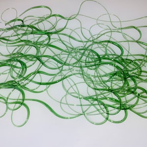May include: Abstract art piece featuring intertwined, translucent green tubes. The tubes are arranged in a flowing, organic pattern, creating a sense of movement and depth. The artwork is set against a plain white background.