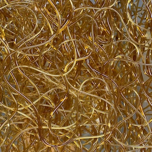 May include: Close-up of a tangled mass of golden, curved tubes. The tubes are smooth and appear to be made of a translucent material, reflecting light and creating a complex, interwoven pattern. The overall effect is abstract and visually intriguing.