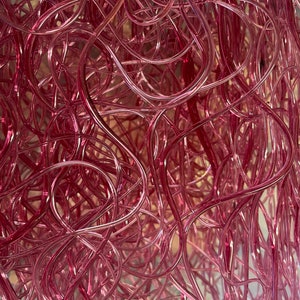 May include: A close-up of a tangled mass of pink glass tubes. The tubes are intertwined and create a complex, abstract pattern.