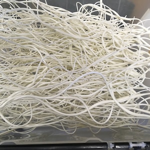 May include: A close-up of a large pile of white, flexible, thin, and long plastic tubes. The tubes are tangled and intertwined.