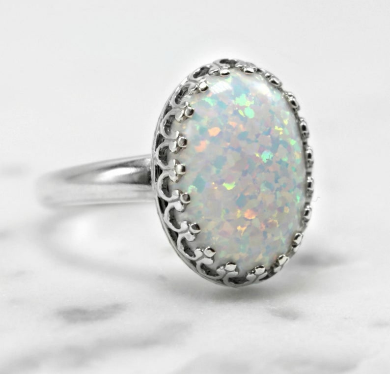 May include: A silver ring with a white opal gemstone set in a delicate filigree design.