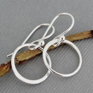 May include: A pair of silver hoop earrings with a simple circle design. The earrings have a small ball at the top of the hoop and a hook closure.
