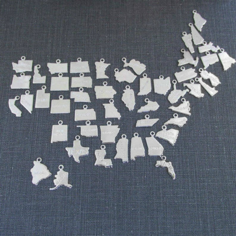 May include: A set of silver charms shaped like the states of the United States. Each charm has a hole at the top for attaching to a necklace or bracelet.