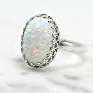 May include: A silver ring with a white opal gemstone set in a delicate filigree design.