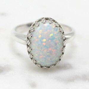 May include: A silver ring with a white opal stone set in a delicate, ornate crown-like setting.