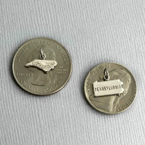 May include: Two silver US quarter coins with state charms. The first coin has a North Carolina charm and the second coin has a Pennsylvania charm.