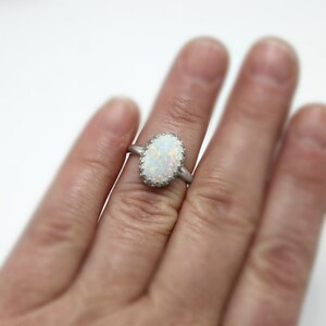 May include: A silver ring with a white oval opal gemstone set in a silver bezel. The ring is on a finger.