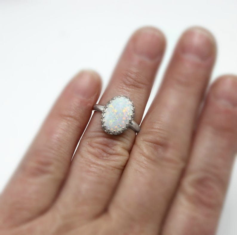 May include: A silver ring with a white oval opal gemstone set in a silver bezel. The ring is on a finger.