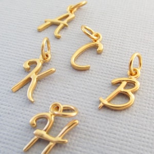 May include: Five gold-coloured cursive letter charms, each with a loop for attaching to a necklace or bracelet. The letters are A, B, C, H, and K.