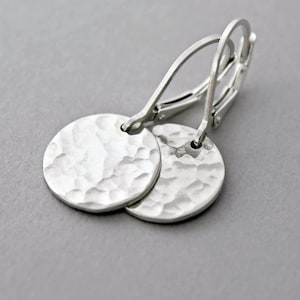May include: Silver hammered disc earrings with lever-back closures. The earrings feature two round, textured silver discs. The hammered texture gives the earrings a unique, handcrafted look. The lever-back closures are visible.