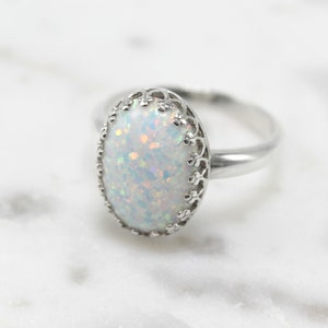 May include: A silver ring with a white opal gemstone set in a delicate filigree design.