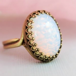May include: A gold ring with an oval-shaped white opal stone set in a decorative filigree design.