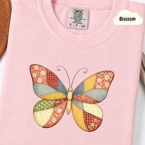 Peut inclure: T-shirt rose clair Comfort Colors avec un motif de papillon patchwork. Les ailes du papillon présentent des motifs floraux, à pois et à carreaux de différentes couleurs. Le mot "Blossom" est dans un nuage blanc.