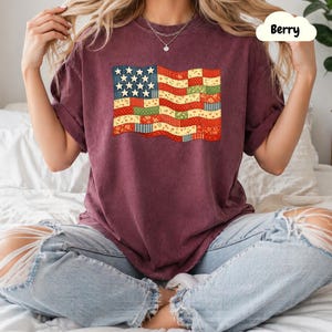 Peut inclure: T-shirt de couleur baie avec un motif de drapeau américain en patchwork. Le drapeau comprend des étoiles et des rayures dans différents motifs et couleurs. Le t-shirt a des manches courtes et une coupe décontractée.