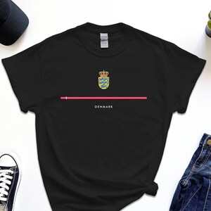 Könnte beinhalten: Schwarzes T-Shirt mit einer roten Linie und dem dänischen Wappen mit dem Text "DENMARK" darunter.