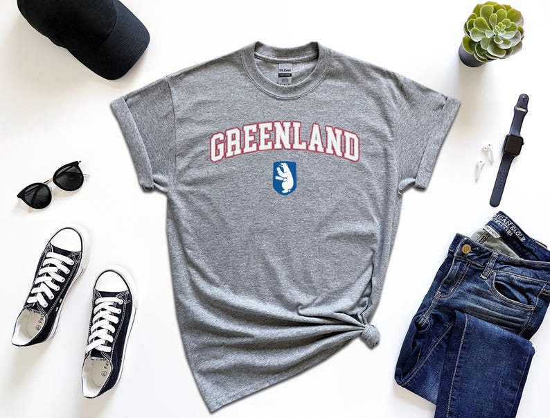 Op de afbeelding: Grijs T-shirt met de tekst "GREENLAND" in rode en blauwe letters met een witte ijsbeer afbeelding.