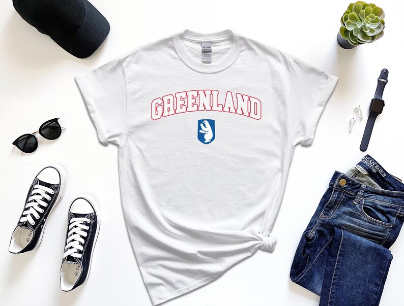 Op de afbeelding: Wit T-shirt met een rode en blauwe grafische afbeelding met de tekst "GREENLAND" en een ijsbeerlogo.