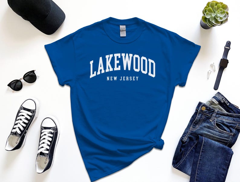 May include: Royal blue t-shirt with the word "Lakewood" arched across the chest in white block letters, with "New Jersey" below. The shirt is surrounded by black sunglasses, black sneakers, a black cap, a watch, and jeans.