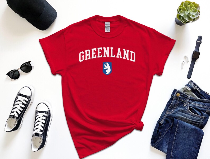 Op de afbeelding: Rood T-shirt met witte tekst "GREENLAND" en een blauwe en witte afbeelding van een ijsbeer.
