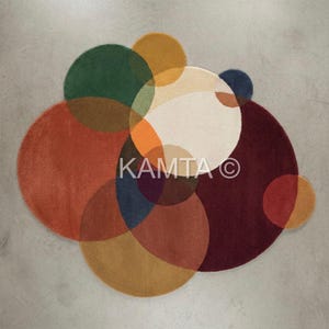 May include: An abstract rug design with overlapping circles in various colours including orange, green, yellow, burgundy, and cream. The rug has a soft texture and the word "KAMTA" is visible.