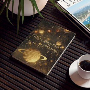 Peut inclure: Une table en bois brun foncé avec une plante dans un pot blanc, un magazine, un journal et une tasse de café. La couverture du journal présente un motif de planète dorée et le texte "My Spiritual Journey". Le magazine est intitulé "TRAVEL MAGAZINE".