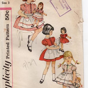 May include: Vintage Simplicity sewing pattern 4135 for a child's dress, size 3. The illustration shows girls in dresses with aprons, holding dolls. The pattern includes the text "Simplicity Printed Pattern 50c". The Bon Marche, Northgate stamp is visible.