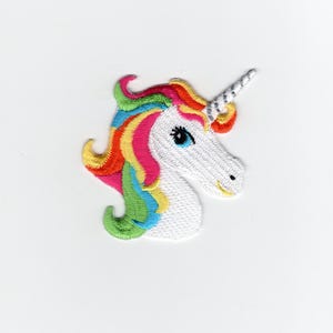 May include: Embroidered unicorn patch featuring a white head with a silver horn and a colorful mane in shades of yellow, orange, pink, blue, and green. The unicorn has a blue eye and a smiling expression. This patch is ideal for adding to clothing or accessories.